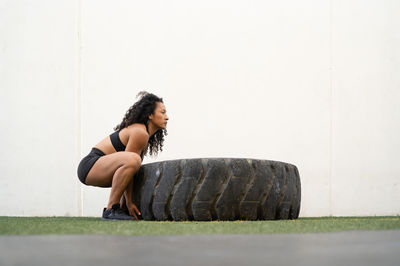 Side view of muscular asian female athlete flipping heavy tire during intense training