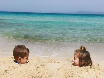 Siblings in sand on shore at beach