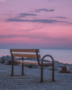 Empty chair on beach against sky during sunset