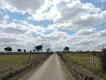 Road passing through field against cloudy sky