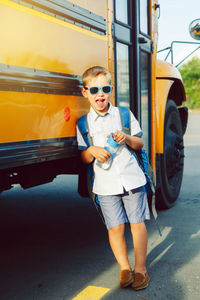 Full length portrait of boy leaning on bus while standing on road