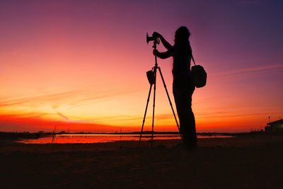 Silhouette person photographing on land against sky during sunset