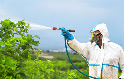 Man holding umbrella by plants against sky