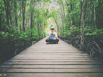 Portrait of man sitting on boardwalk amidst trees