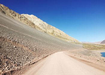 Road amidst desert against clear blue sky