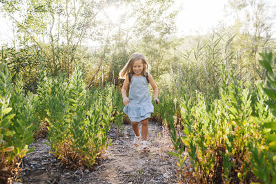 Full length of cute smiling girl running on dirt road amidst plants