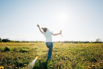 Young girl dancing through a yellow flower field in summer