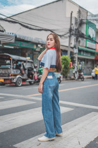 Portrait of young woman standing on road in city