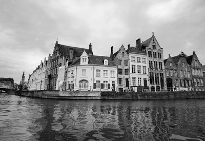 View of buildings by river against cloudy sky