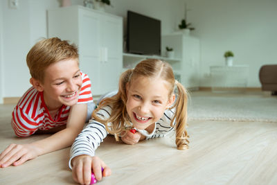 Portrait cheerful siblings playing with dice while lying on carpet at home