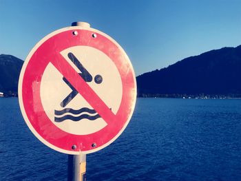 Close-up of warning sign by lake against sky