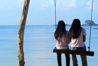 Rear view of girls sitting on beach against sky