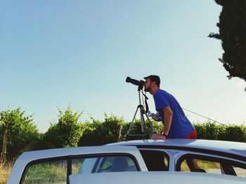 Man photographing car against blue sky