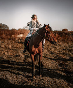 Woman wearing costume riding horse on field