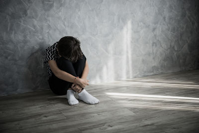 Depressed boy sitting on hardwood floor at home