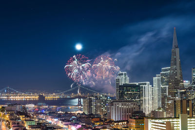 Firework display over illuminated buildings against sky at night