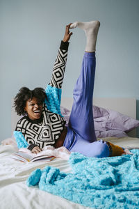 Cheerful hipster woman touching toes while lying on bed at home