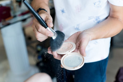 Midsection of make-up artist holding compact powder and brush