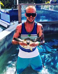 Portrait of man wearing sunglasses standing by swimming pool