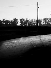 Surface level of wet street by silhouette trees against sky