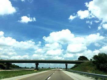 Road passing through trees against cloudy sky