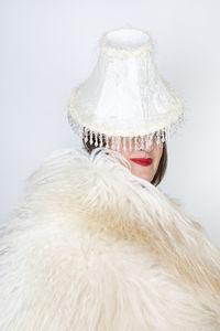 Mature woman in fur with lamp shade on head against white background