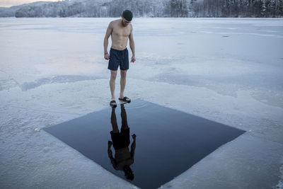 Man standing on frozen lake ready to swim