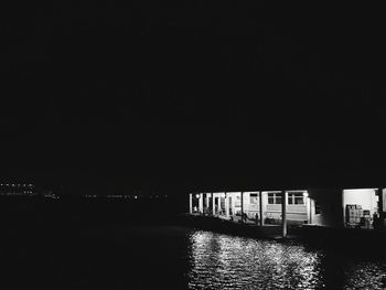 Illuminated city by sea against clear sky at night