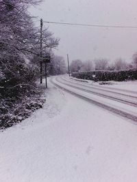 Snow covered road by trees during winter