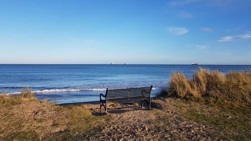 Empty bench on shore by sea against sky