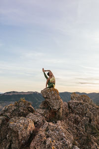 Flexible female in sportswear performing heron pose on top of rocky hill while practicing yoga