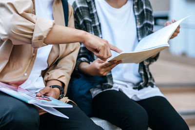 Midsection of people reading book sitting outdoors