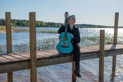 Young woman sitting on pier over lake against sky