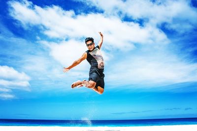 Happy young man jumping at beach against blue sky