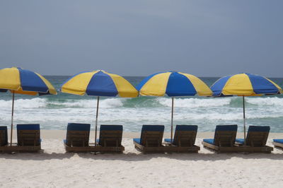 Lounge chairs and parasols on beach against clear sky