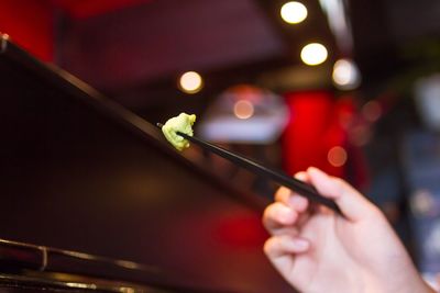 Cropped hand of person eating wasabi with chopsticks
