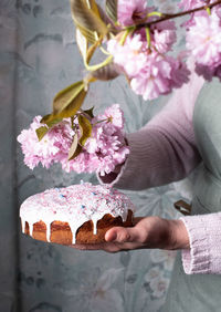 A woman decorates a homemade easter cake with pink sakura flowers,spring blossom