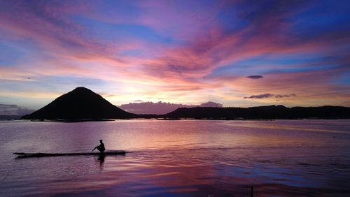 Silhouette person on sea against sky during sunset