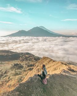 Woman sitting on mountain against cloudscape
