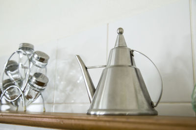 Metallic teapot and salt shakers on shelf against wall in kitchen