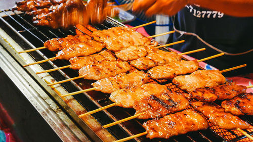 Midsection of vendor cooking kebabs on barbecue grill at market