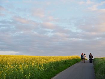 Rear view of people on road amidst field against sky