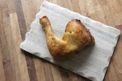 A grilled chicken leg with beautiful crispy skin lies on a wooden board.