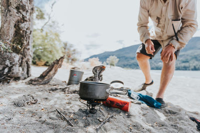 Low section of male hiker preparing food at riverbank