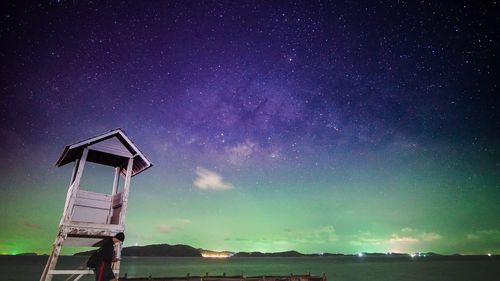 Side view of man standing by lifeguard hut at beach against star field at night