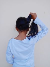 Rear view of girl with hand in hair while standing against white wall