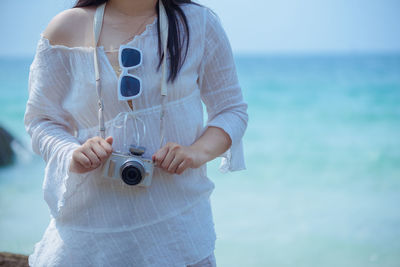 Midsection of woman with camera standing against sea