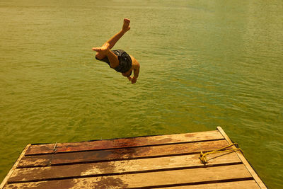 Man jumping on pier over lake