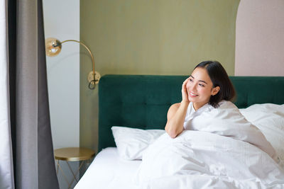 Young woman sitting on bed at home