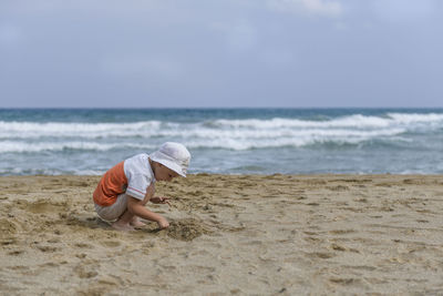 Rear view of boy on beach against sky